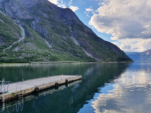 pier on the reflection of the sky and mountains in the blue water of the fjord - Eidfjord