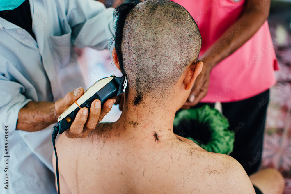 
Close up of Asian man shaving hair for Buddhist ordination ceremony in Thailand. Preparation for new Thai monk.