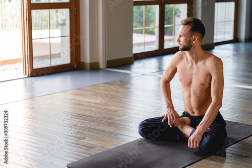 30-35s male yogi sitting peacefully in lotus inside spacious studio with big windows