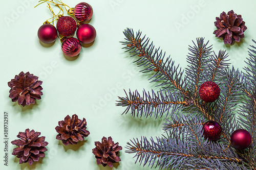 Postcard with a branch of blue spruce with cones and red Christmas balls on a green background, top view with place for text.