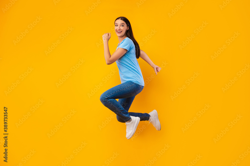 Happy woman jumping over yellow studio wall
