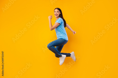 Fototapeta Naklejka Na Ścianę i Meble -  Happy woman jumping over yellow studio wall