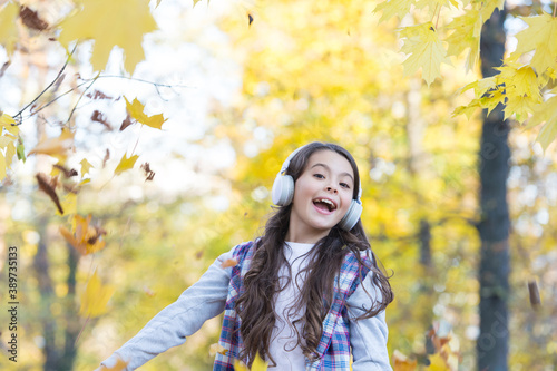 perfect autumn day of cheerful kid listen audio book or music wearing earphones in fall season park play with yellow fallen maple leaves, having fun