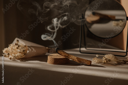  palo santo with jet of smoke, mirror and dried flowers on a neutral background. Abstract trendy picture. Minimalistic wabi sabi style.