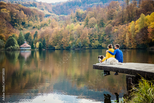couple and dog sitting by beautiful autumn lake