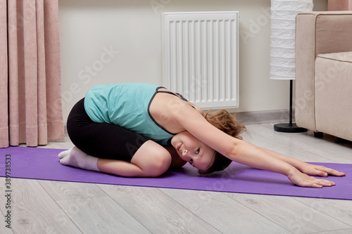 Cute beautiful girl doing exercises for body flexibility at home. Sports lifestyle.