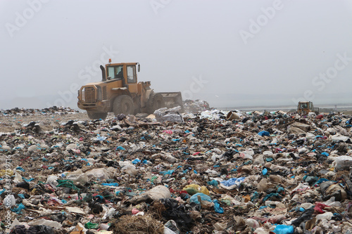 An excavator and a compactor working on a dusty sanitary landfill