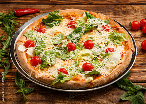 Caesar pizza with salad and tomatoes on wooden background