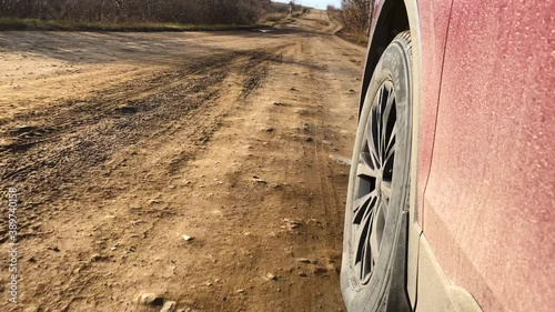 Video shooting in motion, driving a dirty red car on a dirt road at speed, view from behind the steering wheel. The car's wheel is spinning. photo