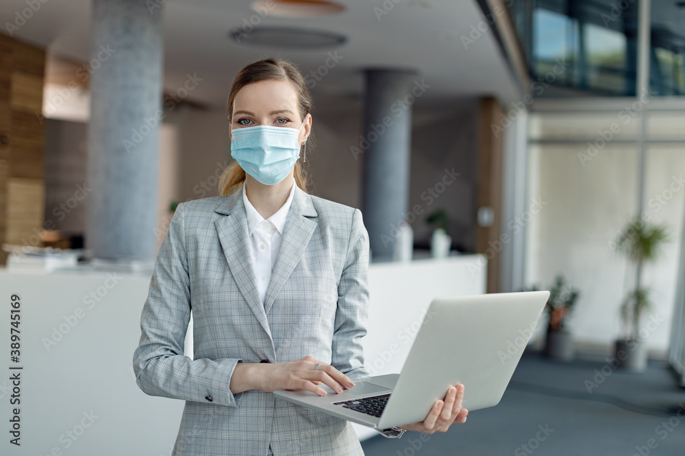 Young businesswoman with face mask working on laptop and looking at camera. Young businesswoman with face mask working on laptop and looking at camera.