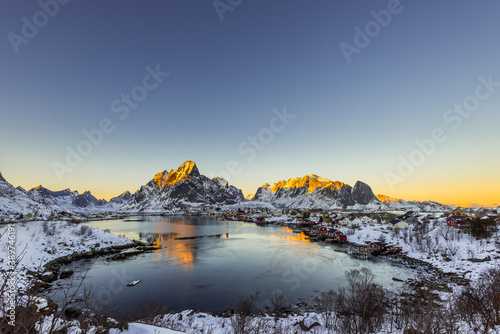 The small fishing village Reine on the Lofoten islands in Norway in winter with steep snowcapped mountains and frozen lake during sunset photo