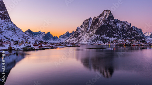 The small fishing village Reine on the Lofoten islands in Norway in winter with steep snowcapped mountains and frozen lake during sunset