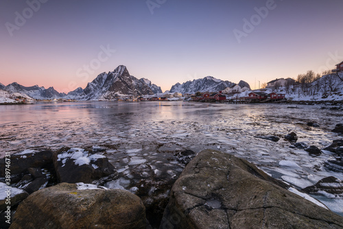 The small fishing village Reine on the Lofoten islands in Norway in winter with steep snowcapped mountains and frozen lake during sunrise photo