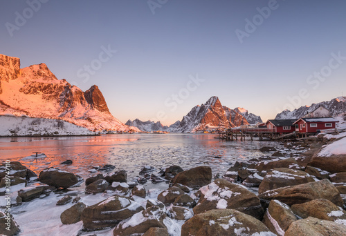 The small fishing village Reine on the Lofoten islands in Norway in winter with steep snowcapped mountains and frozen lake during sunrise photo