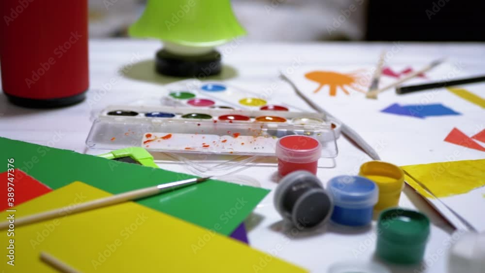 Watercolors, Paper, Brushes Randomly Laid Out on Table. Brush in Hand of Child Watercolors, Paper, Brushes Randomly Laid Out on Table. Brush in Hand of Child