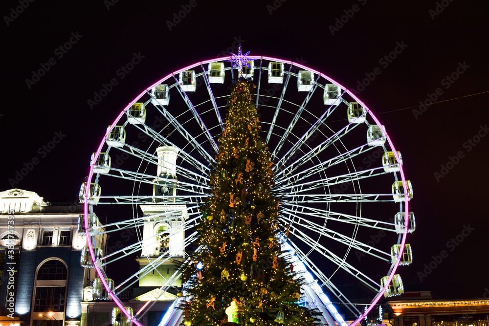 Christmas city tree against the background of the illuminated Ferris wheel.