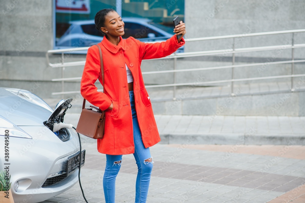 Obraz premium African American girl charging electro car at the electric gas station