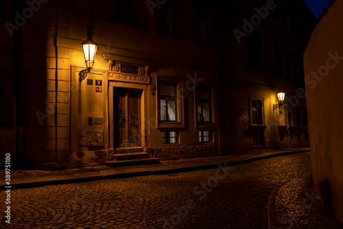 
light from street lights and a paved sidewalk made of cobblestones in a street in the old town of prague at night