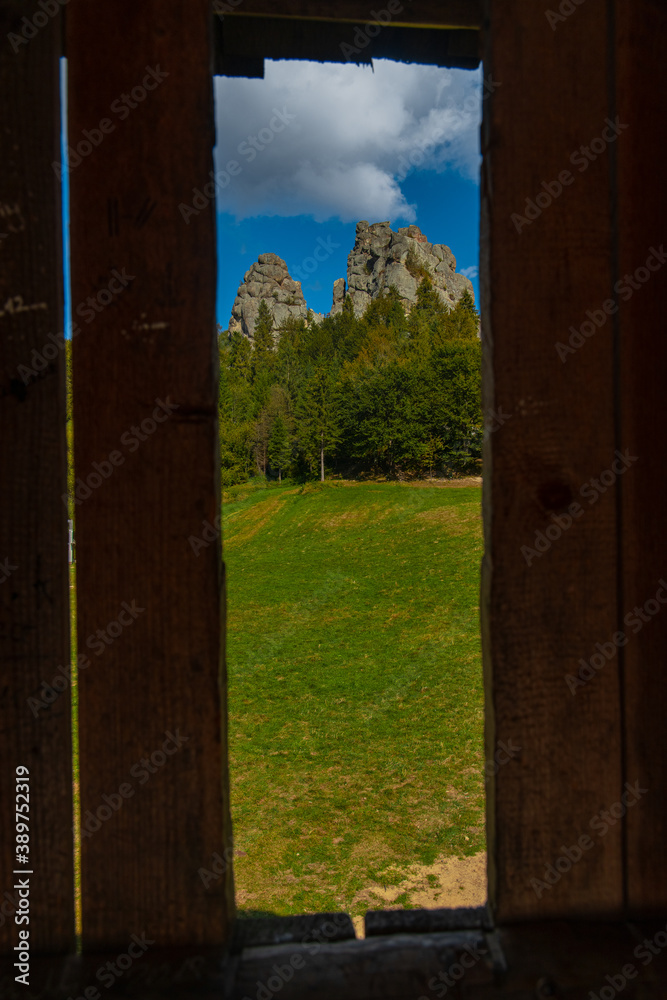 vertical picture of summer clear weather day time landscape scenic view on stone mountain rock peaks above green trees in wooden frame foreground