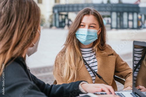 Two young friends wearing face masks and working together in a coffee shop