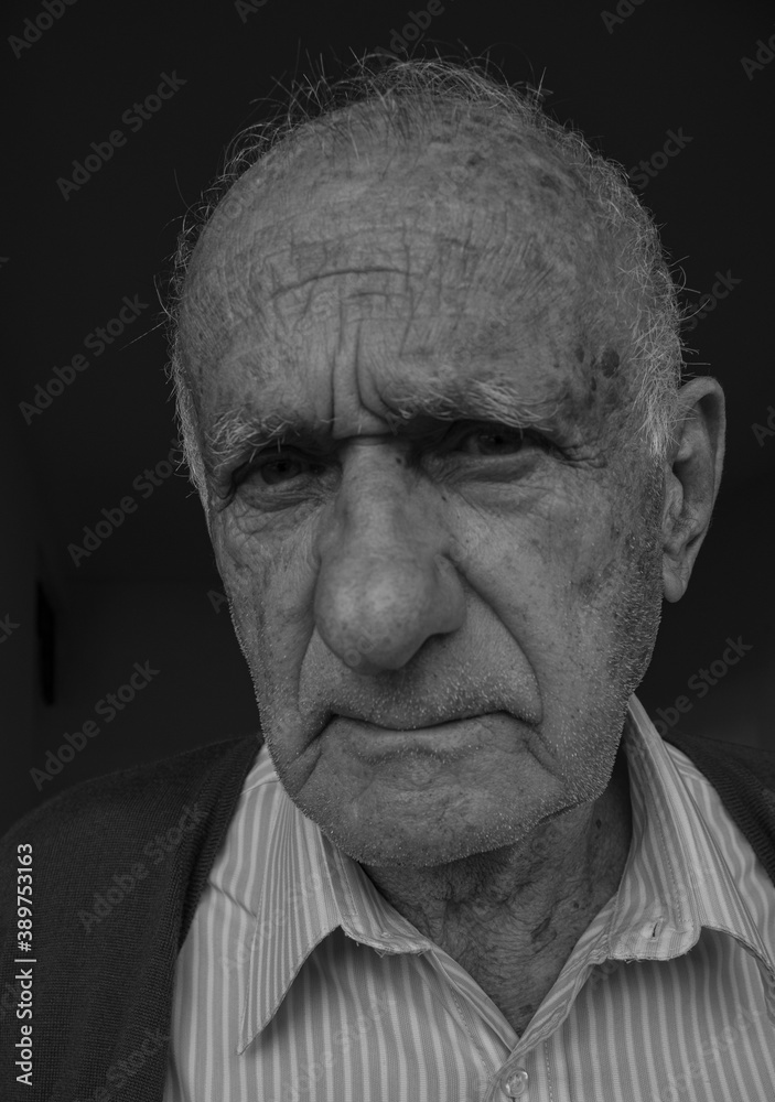 White old man, wrinkled, seroius, with a sad eyes, looking at the camara in black and white. Alone and mad man.