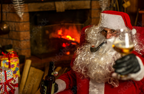 Santa makes the toast for the holiday season with beer. Fireplace background on
