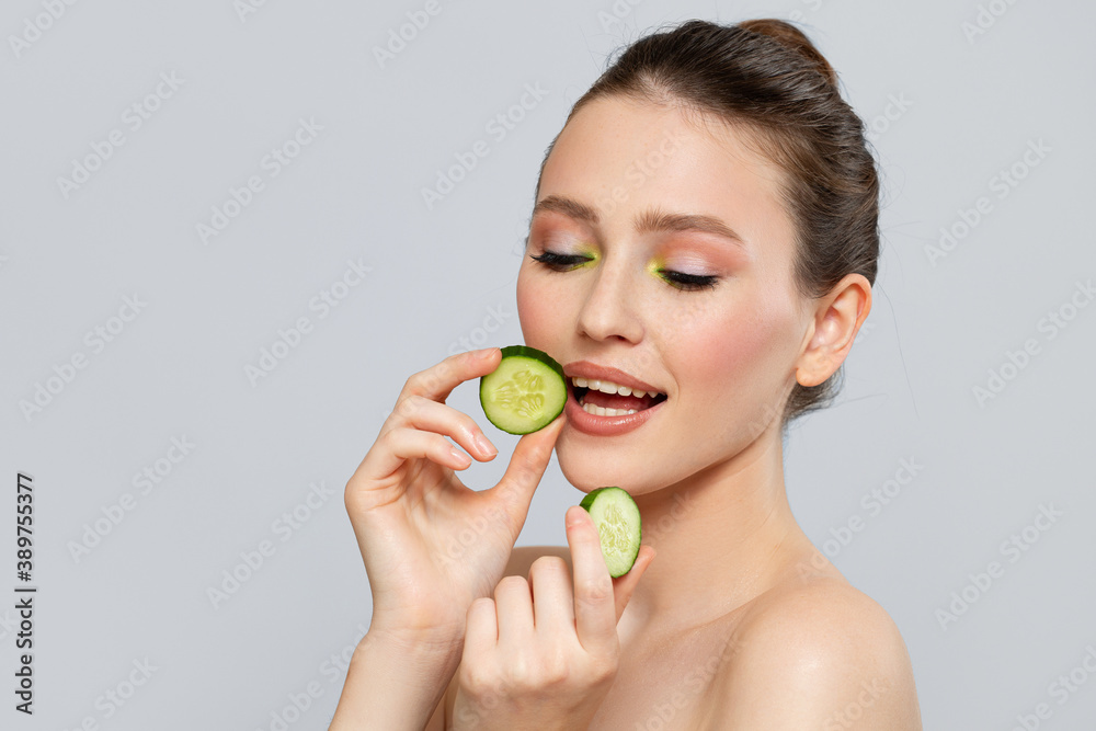 Beautiful young smile woman holding fresh cucumber slices. Skin care, spa, natural beauty and cosmetology concept, on gray copyspace background Beautiful young smile woman holding fresh cucumber slices. Skin care, spa, natural beauty and cosmetology concept, on gray copyspace background