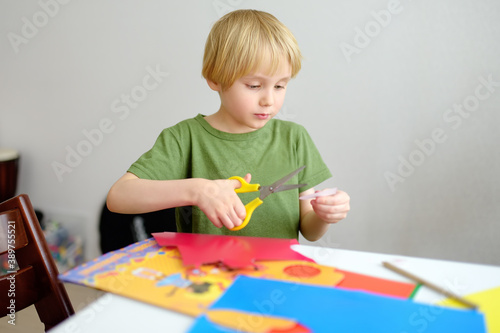 Little boy making colored paper crafts at home. Child cuts scissors details. Creativities lessons, distance learning, homeschooling for kids.