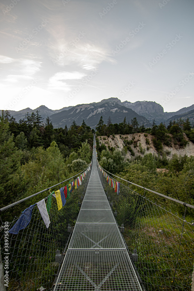 Wooden long footbridge above the deep gorge with a river beach at the bottom, between the rocks. Wild mountains in Swiss Alps