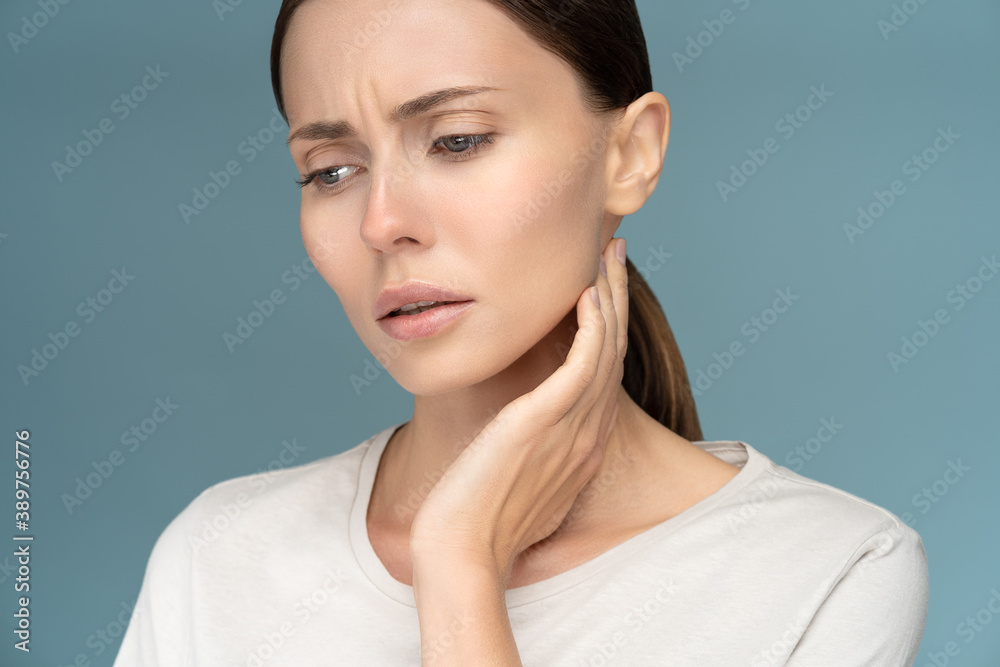 Closeup of sick sad woman checking lymph nodes, caught cold, suffering from throat problems, isolated on studio blue background Closeup of sick sad woman checking lymph nodes, caught cold, suffering from throat problems, isolated on studio blue background