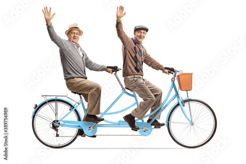 Elderly men riding a blue tandem bicycle and waving at camera