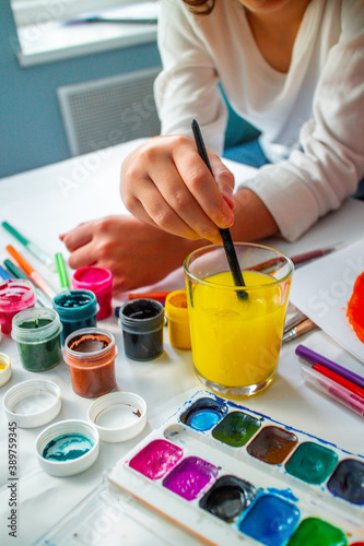 The child lowers his hand into the delta water, washing off the gouache. Home schooling. Drawing training. Children's independence of art. High quality photo