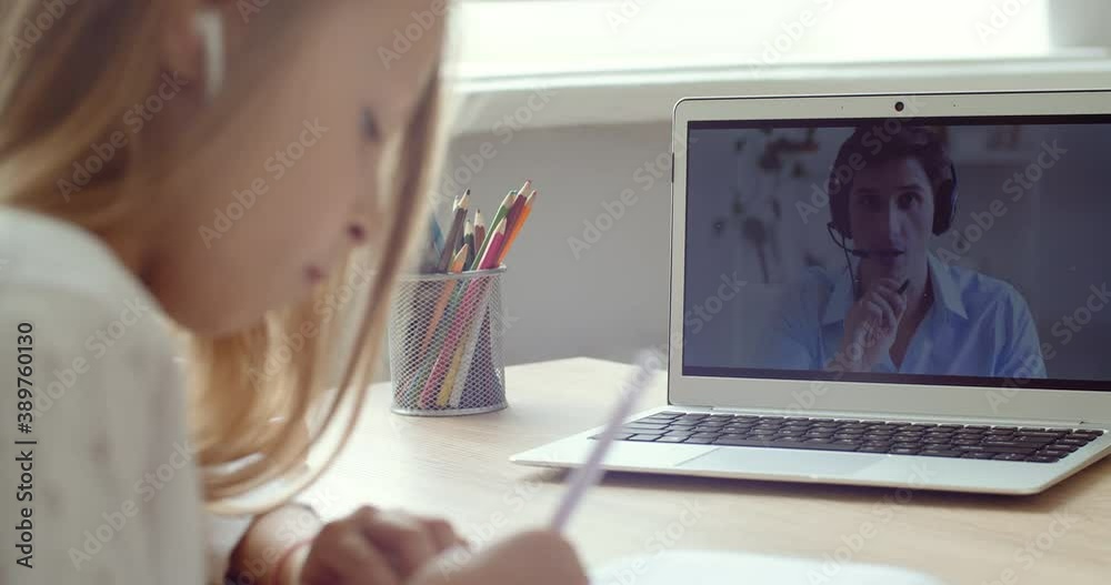 Side view caucasian primary school girl wearing headphones look at laptop screen distance learning at home. Focused cute kid listening audio lesson online video studying at table doing homework remote Side view caucasian primary school girl wearing headphones look at laptop screen distance learning at home. Focused cute kid listening audio lesson online video studying at table doing homework remote