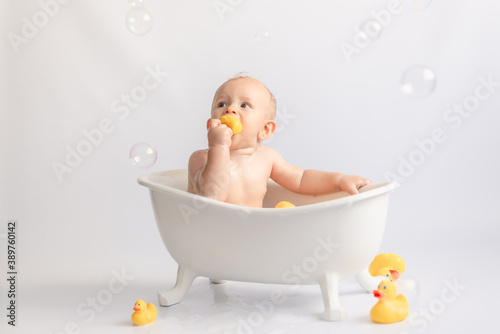 bathing the baby in white bath with foam and rubber ducks