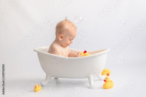 baby bathing toddler in white bath with foam