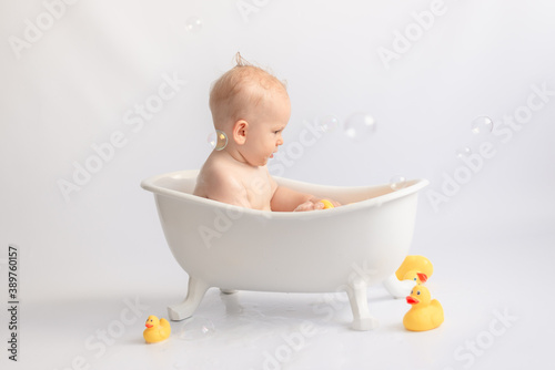 Fényképezés bathing the baby in white bath with foam and rubber ducks