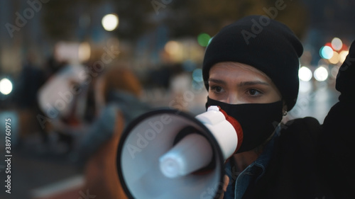  young woman with face mask shouting slogans to loudspeaker at street protest . High quality photo