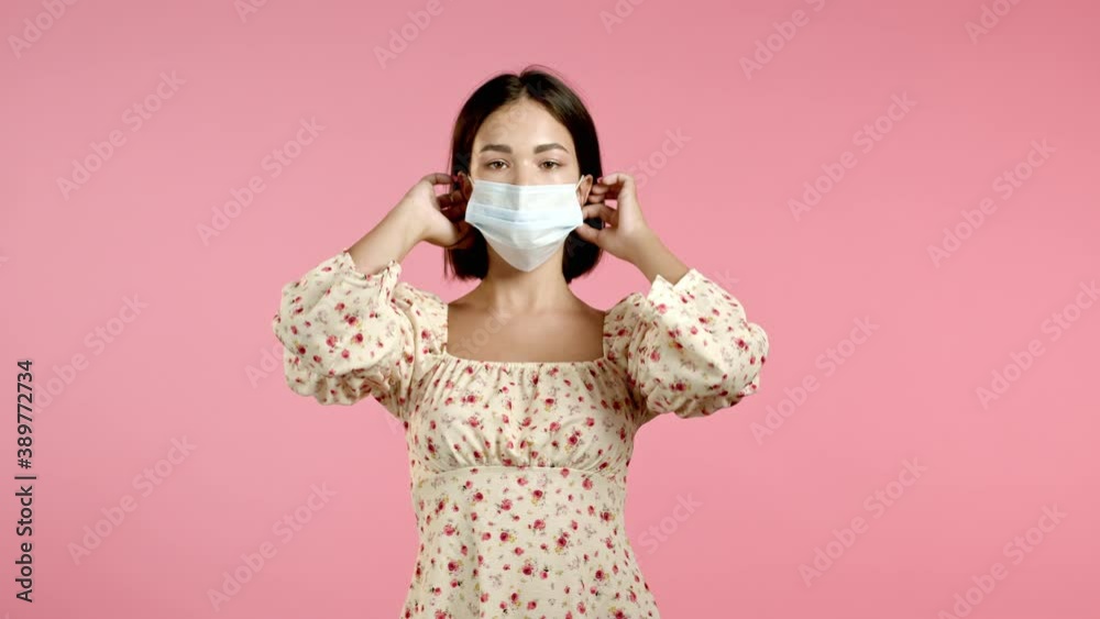 Young pretty woman puts on face medical mask during coronavirus pandemic. Portrait on pink background. Protection with respirator against COVID-19 outbreak Young pretty woman puts on face medical mask during coronavirus pandemic. Portrait on pink background. Protection with respirator against COVID-19 outbreak