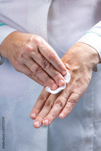 female nurse or doctor using alcohol liquid to make disinfection of her hands before medical procedure. medic washing hands. female wearing doctor smock