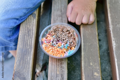 Small ice cream multi-colored ice cream balls in a cup on a bench. Next to the child's hand.