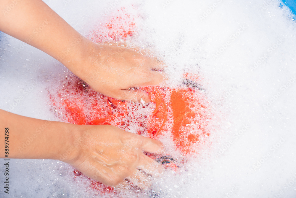 Fototapeta premium Closeup young Asian woman use hands washing color clothes in basin with detergent have soapy bubble water, studio shot background, laundry concept
