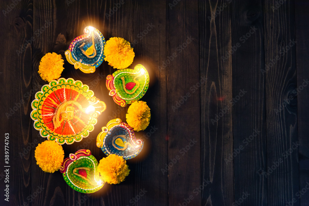 Top view overhead clay lit light a fire already on Diya or oil lamp, studio shot on black wooden background, Decoration of Hinduism rangoli, Happy celebration Deepavali or Diwali festival concept
