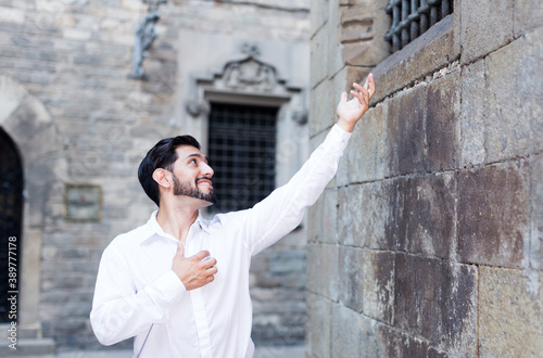 Handsome bearded man standing near stone wall singing serenade to his beloved