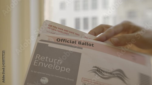Close-up on woman's hand putting an official election ballot into an envelope for the November 2020 United States local and federal elections. Slow motion with shallow focus, recorded in 4K UHD at 120