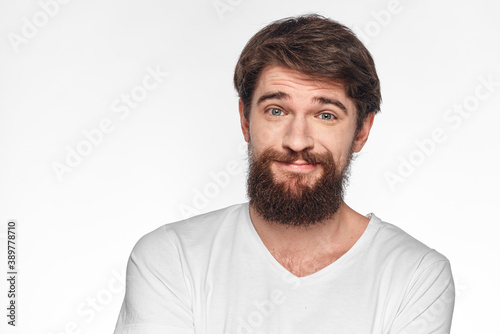 cheerful bearded man in a white t-shirt emotions gestures with his hands light background studio