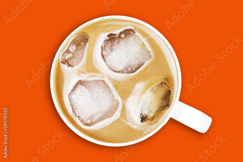 Ice coffee top view. Frozen latte with ice cubes. White ceramic cup isolated on orange. Sweet sugar beverage milk drink.