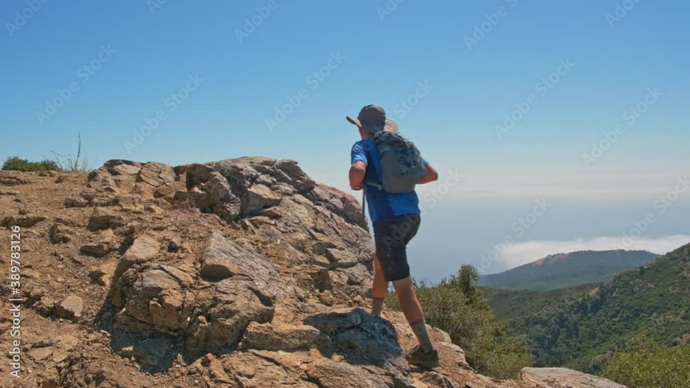 Man hikes to rocky summit and kneels to admire the view Man hikes to rocky summit and kneels to admire the view