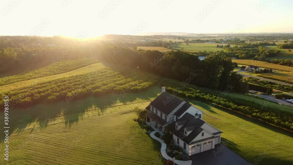 Countryside estate home set among rural farmland and orchard meadow during sunrise. Peaceful house on hillside overlooking green lush land in small town America.