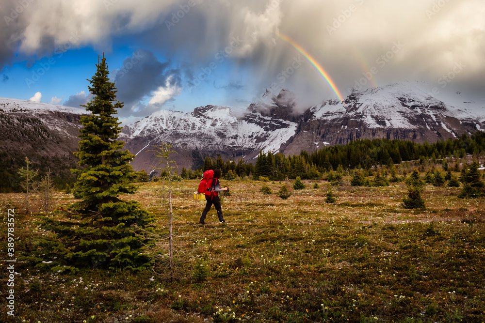 Female Backpacker Hiking in Canadian Rockies. Colorful Dramatic Sky with Rainbow Art Render. Taken near Sunshine Village and Banff, Alberta, Canada.