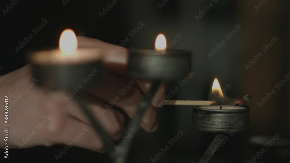 Close up of a lit match stick igniting multiple tealights in a silver candle holder with a dark background a night. Shot in 4K.